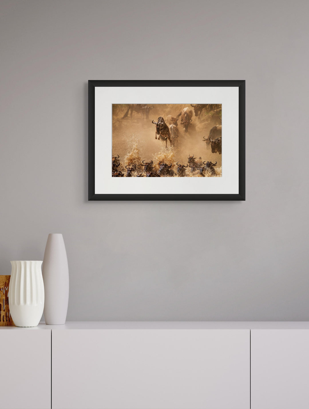 Fine art framed photograph: In the wild, wildebeest embark on a daring journey through the Mara River. One defies gravity, leaping above the herd, embodying the untamed essence of the savannah. By Edith Garneau