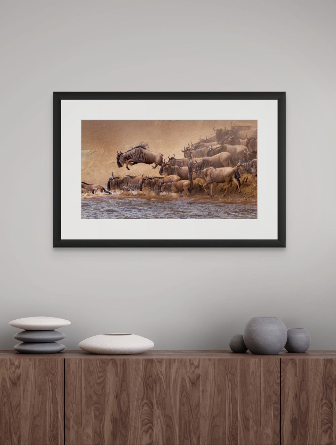 Fine art framed photograph: In the Serengeti's wildebeest migration, the Mara River crossing captivates. A lone wildebeest airborne, embodying the wild pulse of nature's symphony in this extraordinary spectacle. By Thomas Nicholson